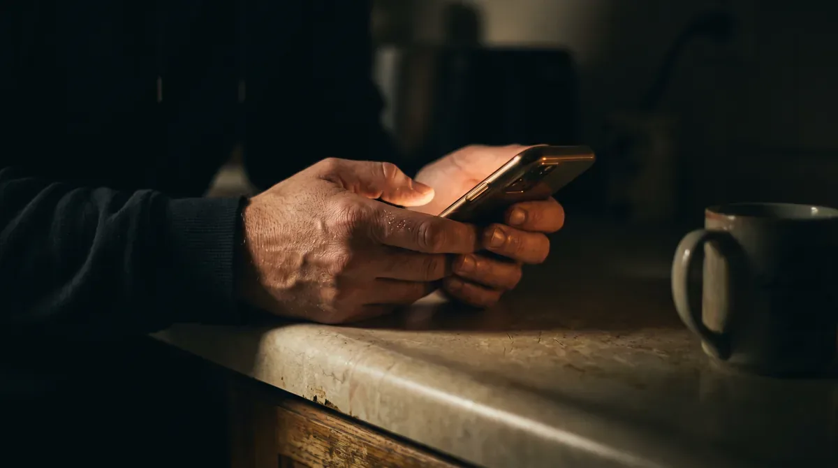 Two hands using a phone late at night, the screen the only light in the room